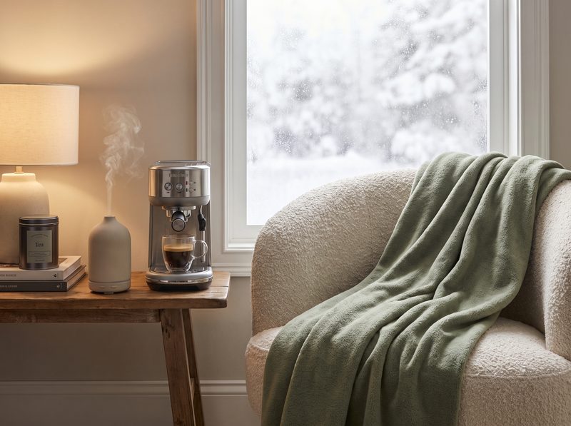 Sage green fleece throw on a boucle armchair beside a misting diffuser and compact coffee machine