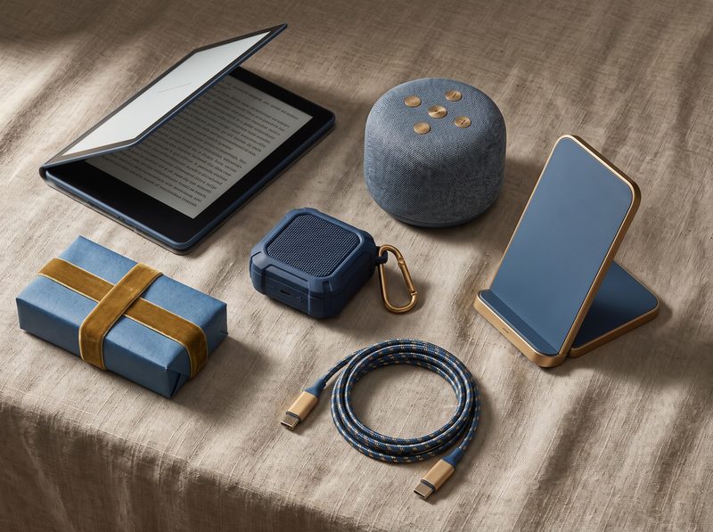 Flat lay of an e-reader, small smart speaker, clip speaker and foldable wireless charger on linen