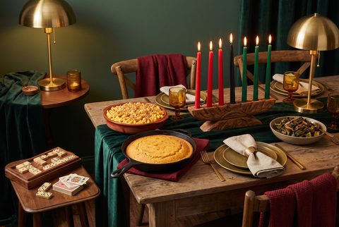 Sunday dinner and Kwanzaa table with a wooden kinara holding red, black and green candles, cornbread in a cast iron skillet, dominoes and playing cards