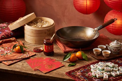 Lunar New Year table with stacked bamboo steamers, a wok, red envelopes, mandarins, a gongfu tea set and mahjong tiles