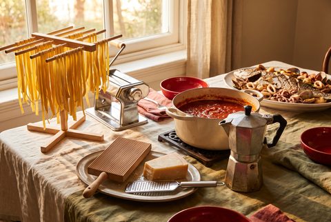 Italian American Sunday dinner table with fresh pasta drying on a rack, a hand-crank pasta machine, a pot of red sauce and a moka pot