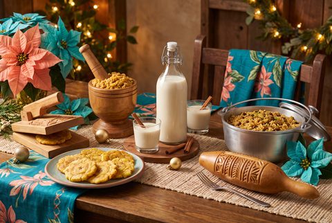 Parranda table with glasses of creamy coquito and cinnamon sticks, a wooden pilón with mofongo, tostones, a caldero of arroz con gandules and a güiro