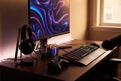 Gaming desk with a glowing monitor, a headset on a stand, an RGB keyboard, a controller and a wrapped gift