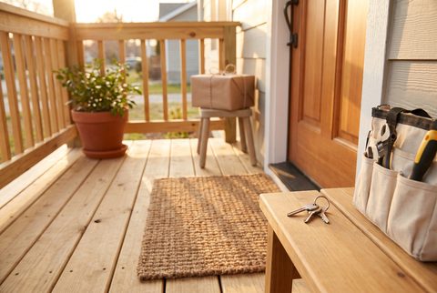 Front porch with a jute doormat, a potted plant, house keys on a bench, a tool bag and a wrapped gift