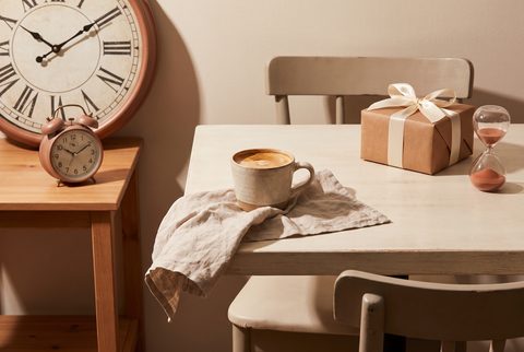 Cafe table with an empty chair, a coffee cup, an hourglass, clocks and a wrapped gift