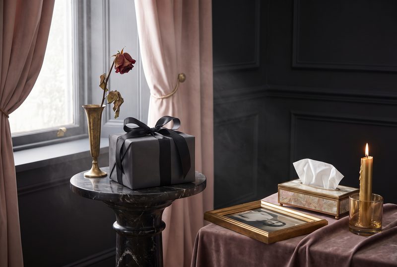 Moody windowsill with a single rose, a wrapped gift, a tissue box and a candle