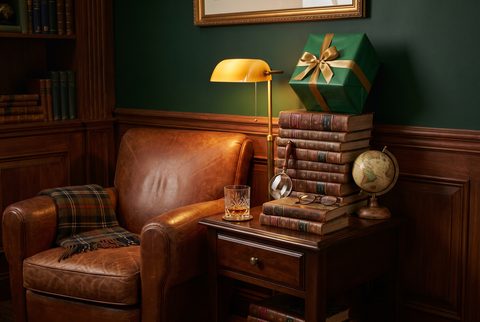 Leather armchair beside stacked encyclopedias, a globe, a magnifying glass and a wrapped gift