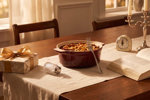 Holiday dinner table with a casserole, a knocked-over salt shaker, a cookbook, a kitchen timer and a wrapped gift