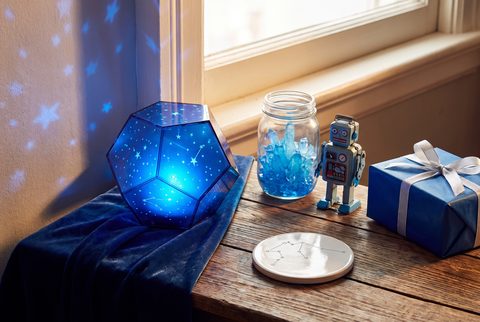 Glowing blue star projector on a velvet cloth beside a jar of blue crystals, a toy robot, a coaster and a blue wrapped gift