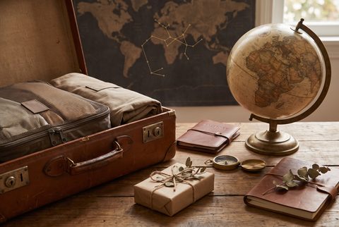 Open vintage suitcase with packing cubes beside a globe, a travel journal and a wrapped gift, with a world map on the wall