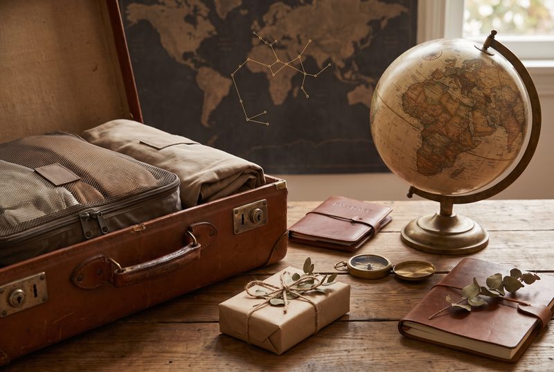 Open vintage suitcase with packing cubes beside a globe, a travel journal and a wrapped gift, with a world map on the wall